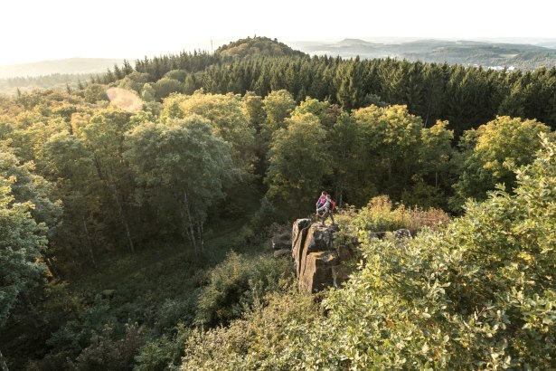 Zwei Personen stehen auf einem Felsen, umgeben von einem dichten Wald. Im Hintergrund sind Hügel und ein weiter Blick über die Landschaft zu sehen., © Eifel Tourismus GmbH, D. Ketz Zwei Personen stehen auf einem Felsen, umgeben von einem dichten Wald. Im Hintergrund sind Hügel und ein weiter Blick über die Landschaft zu sehen., © Eifel Tourismus GmbH, D. Ketz