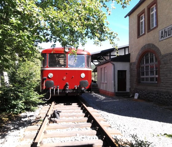 Historischen roten Eisenbahn vor dem Museumsbahnhof Ahütte.
, © Andreas Kurth Eine historischen roten Eisenbahn steht auf Gleisen neben einem alten Bahnhofsgebäude mit der Inschrift "Ahütte" an der Wand.
