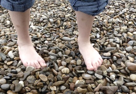 Zwei nackte F&uuml;&szlig;e stehen auf einem Kieselstrand. Die Person tr&auml;gt hochgekrempelte Jeans., &copy; pixabay