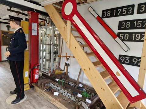 Un musée avec un conducteur historique et une grande échelle rouge sur le mur. À l'arrière-plan, on peut voir des escaliers et diverses antiquités.