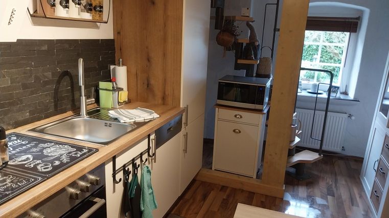 Een moderne keuken met hout- en roestvrijstalen elementen. De ruimte is licht en goed gestructureerd met een wenteltrap op de achtergrond.