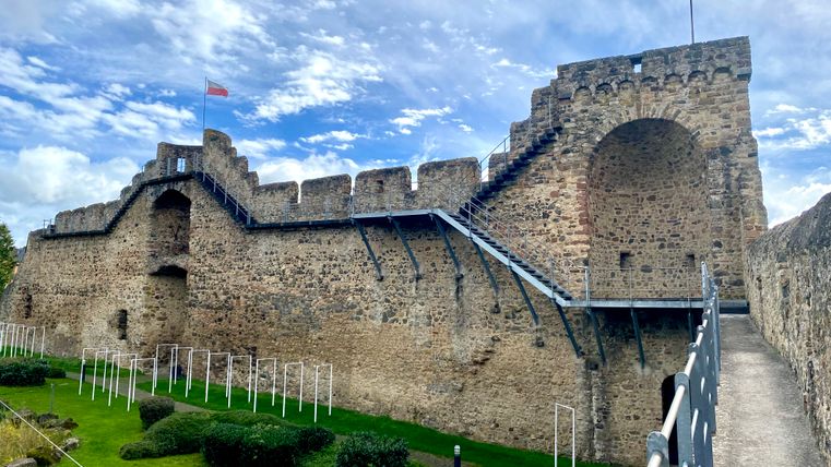 Begehbare hohe Stadtmauer aus Stein in Hillesheim mit angrenzender Parkfläche.