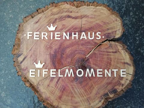 A wooden sign with the inscriptions "Holiday Home" and "Eifel Moments". It is made of natural wood and has a rustic appearance.