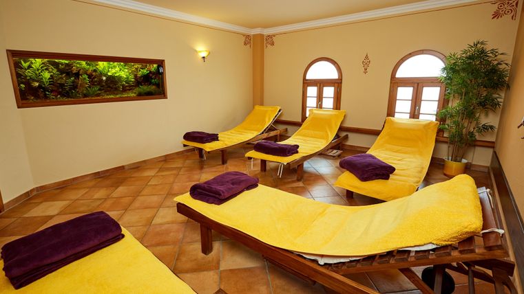 Wellnessraum mit gelben Liegen, lila Handtüchern, Aquarium und Pflanzen. Entspannende Atmosphäre.