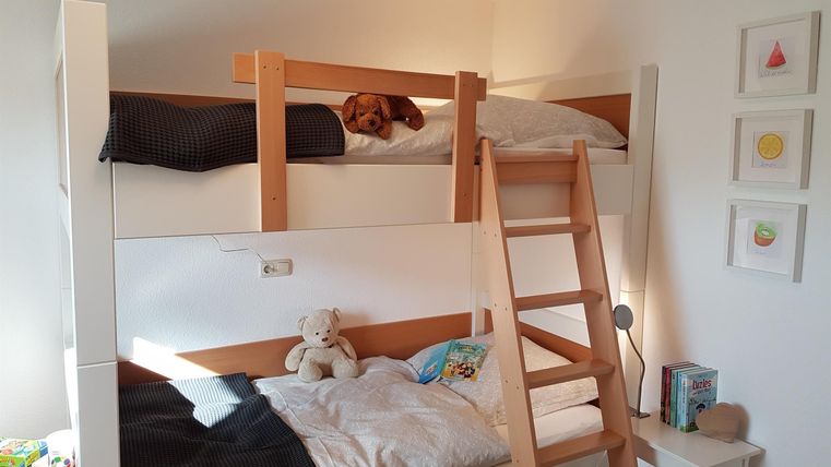 Ein helles Kinderzimmer mit einem Etagenbett und einer Treppe. Auf der oberen Matratze liegt ein Hund und eine weiche Decke auf dem unteren Bett.