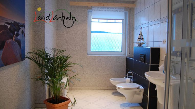 Ein modernes Badezimmer mit einem Fenster, einer Pflanze in einem Topf und stilvollen Sanitäranlagen. Die Wände sind hell gefliest und bieten eine angenehme Atmosphäre.