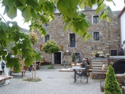 Innenhof einer historischen Mühle mit Steinmauern, Tischen und Pflanzen. Menschen sitzen an Tischen, umgeben von grünen Blättern und rustikalen Dekorationen.