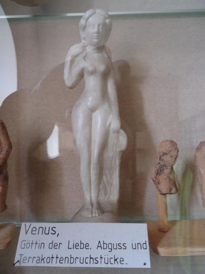 Kleine Statue der Venus, Göttin der Liebe, ausgestellt in einem Museum. Beschriftung: "Venus, Göttin der Liebe. Abguss und Terrakottenbruchstücke."