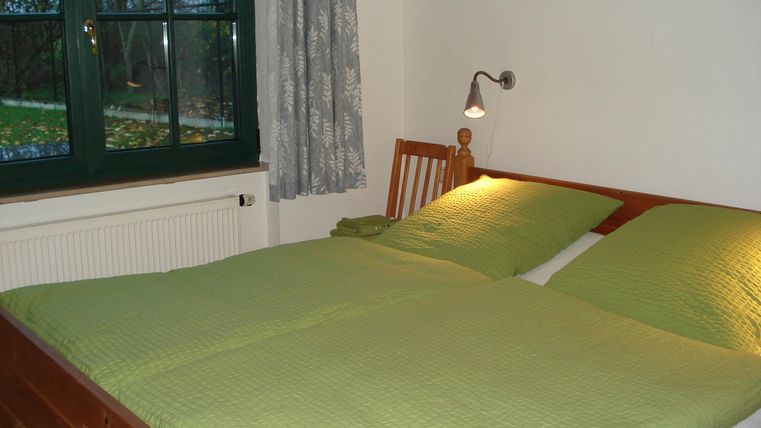 Een gezellige slaapkamer met een tweepersoonsbed en groen beddengoed. De kamer heeft een raam met uitzicht op een rustige tuin.