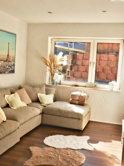 Een gezellige woonkamer met een beige bank en een vensterbank. Op de achtergrond is een afbeelding van de Eiffeltoren en decoratieve planten te zien.