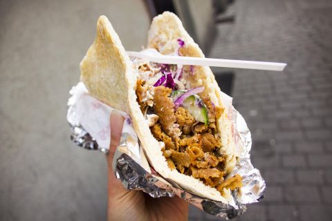 Ein Döner in einer Hand gehalten, gefüllt mit Fleisch, Salat und Soße, in Alufolie eingewickelt.