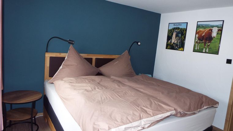 Ein gemütliches Schlafzimmer mit einem großen Bett und zwei Kissen. Die Wände sind in einem beruhigenden Blauton gestrichen und es hängen Bilder an der Wand.