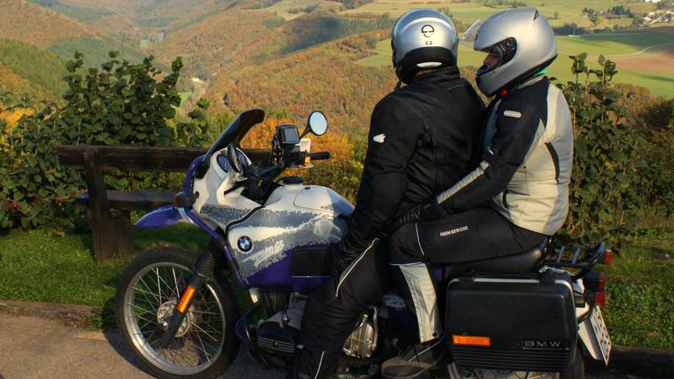 Deux motards sont assis sur une BMW à un point de vue. En arrière-plan, un paysage pittoresque s'étend avec des collines douces.