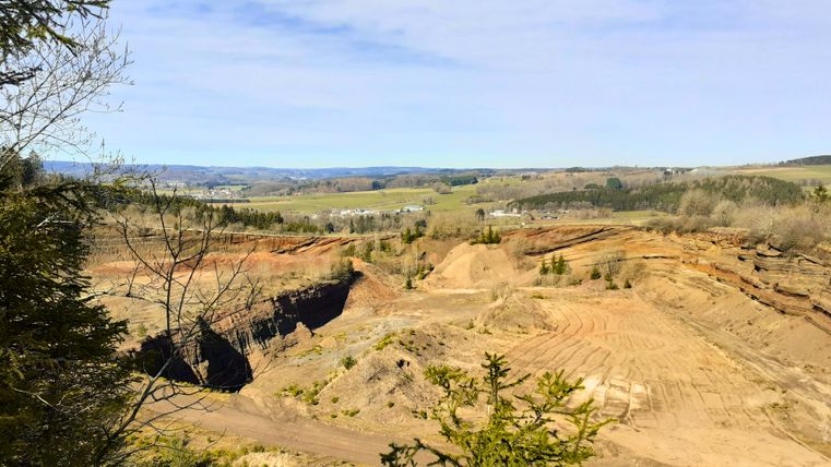 Blick auf eine hügelige Landschaft mit einem Steinbruch und Bäumen im Vordergrund.