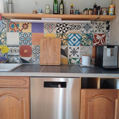 Een moderne keuken met een kleurrijke tegelwand en houten kasten. Op het aanrecht staan enkele keukengerei en apparaten.