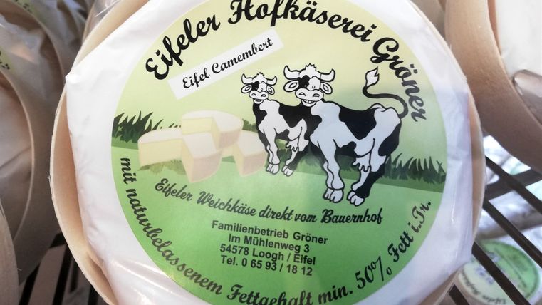 Ein Laib Camembert der Eifeler Hofkäserei Gröner mit Foto zweier Kühe auf der Verpackung, Adresse des Herstellers und Angaben zum Fettgehalt.