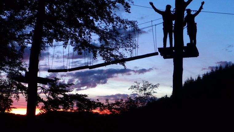 zwei sich freuende Menschen auf Zipline Plattform in Abenddämmerung</p>
