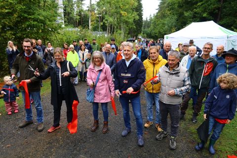 Fünf Personen mit Scheren in den Händen durchschneiden gleichzeitig ein rotes Band. Hinter ihnen zahlreiche Zuschauer und Kinder.