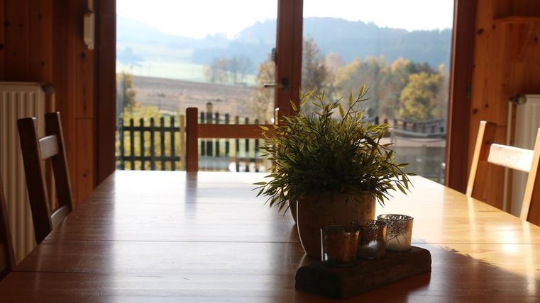 Ein heller Essbereich mit einem Holztisch und Blick auf die Natur. Auf dem Tisch steht eine Pflanze und einige dekorative Kerzen.