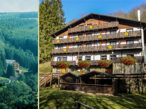 Ein gemütliches Hotel im Grünen mit Balkonen und blühenden Blumenkästen. Im Hintergrund sind bewaldete Hügel zu sehen.