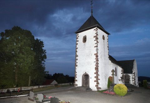 Die Wehrkirche Berndorf steht bei Dämmerung im Mittelpunkt, umgeben von Bäumen und einem Friedhof. Der Himmel ist dunkelblau gefärbt.