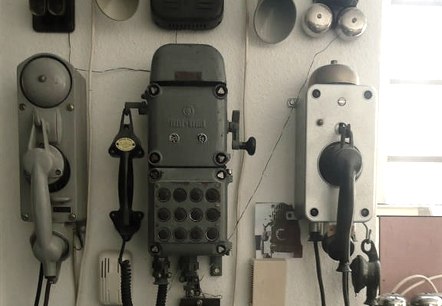 Talrijke telefoonmodellen uit verschillende tijdperken hangen naast en boven elkaar aan een muur.