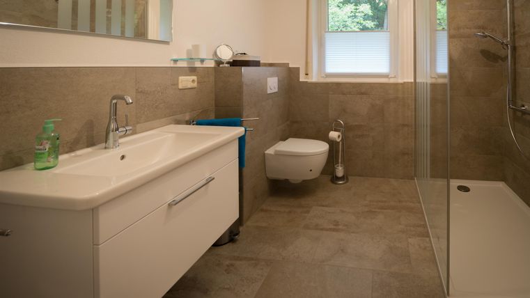A modern bathroom with neutral tiles and a shower. There is a sink and a toilet in a light design.