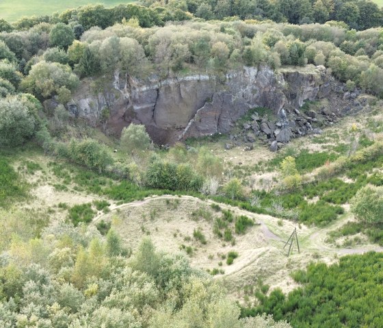Aerial view of the wooded area with the rock face of the Steffelberg and green meadows. A path winds its way through the landscape., © Touristik GmbH Gerolsteiner Land, Sarah Wiesen