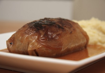Eine Kohlroulade in einer Backform mit Sauce und Kartoffelpürree daneben