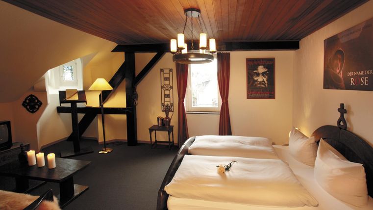 Une chambre confortable avec deux lits et un design en bois chaleureux. La pièce est décorée avec une lampe, une table et un poster, ce qui crée une atmosphère relaxante.