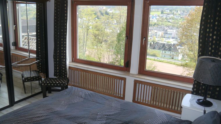 Ein gemütliches Schlafzimmer mit großen Fenstern und Ausblick auf die Umgebung. Der Raum ist stilvoll eingerichtet mit einem Bett und einem Stuhl.