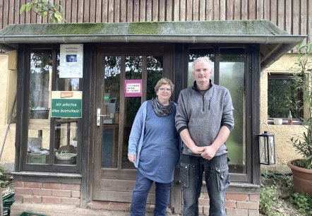 Ein Mann und eine Frau stehen vor einem Geb&auml;ude und l&auml;cheln in die Kamera.