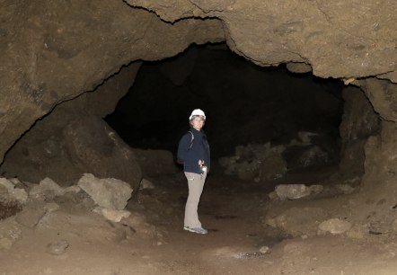 A woman wearing a helmet and carrying a torch in a large stone cave.
