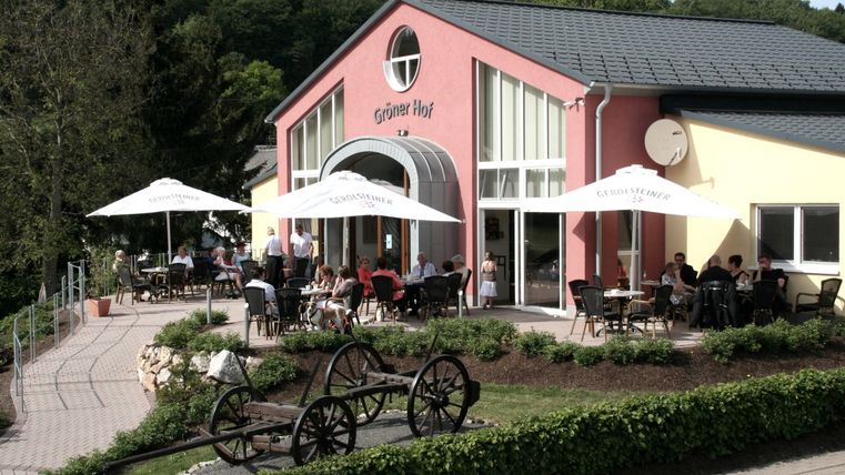 Außenfassade Restaurantgebäude des Gröner Hofs mit zahlreichen Besuchern an Tischen und unter Sonnenschirmen auf der Terrasse.