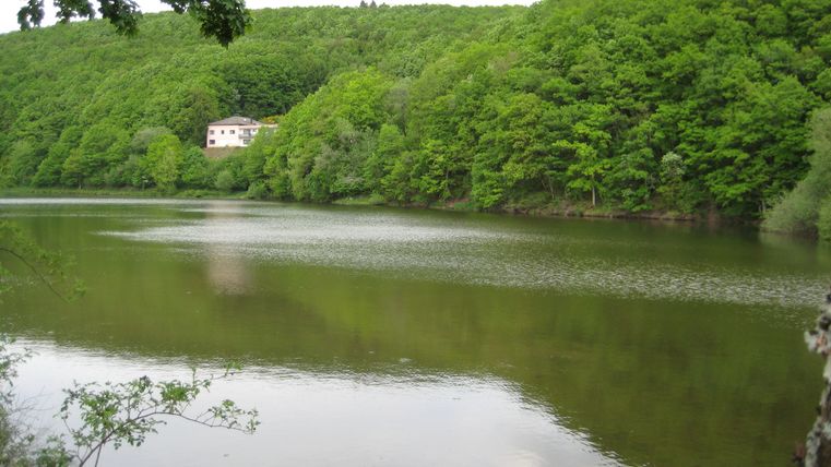 Ein See mit bewaldeten Hügeln im Hintergrund und einem Gebäude am Ufer.