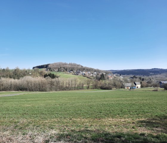 Eine blühende hügelige Landschaft mit grünen Wiesen und einem Dorf in Sichtweite.