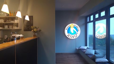 Eingangsbereich des Kinos mit Theke, Kaffeemaschine, Preistafel und beleuchtetem Kinoschild. Sitzbank mit Kissen am Fenster.