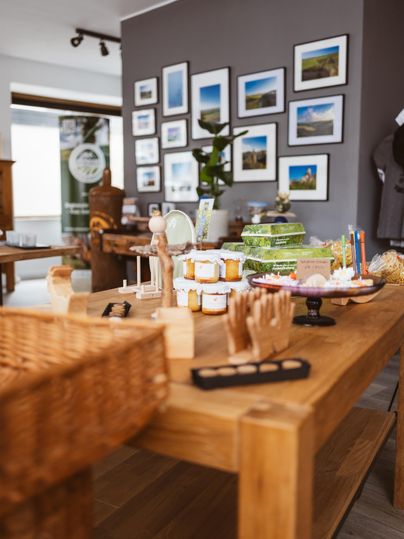 Une vitrine avec des pots de confiture, des boîtes-cadeaux et des images au mur. Une table en bois est chargée de différents produits.