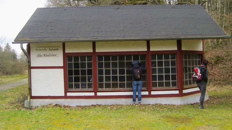 Twee mensen kijken naar een oud gebouw met grote ramen en een bord met de tekst 'Old winch house'.