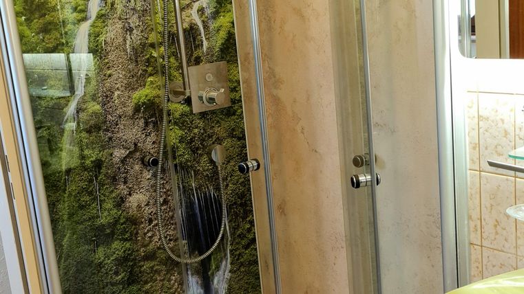 A modernly designed bathroom with a shower and a beautiful wall mural of a waterfall. The amenities include a small sink and bright tiles.