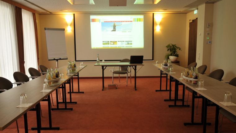 Une salle de conférence avec de nombreuses chaises et tables. Un écran avec une présentation est accroché au mur.