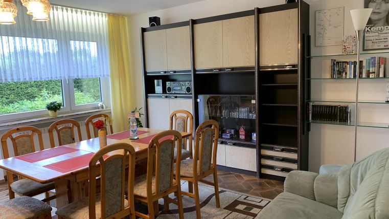 Ein einladendes Wohnzimmer mit einem großen Essbereich und einer modernen Möbelwand. Es gibt viel Tageslicht und eine gemütliche Atmosphäre.