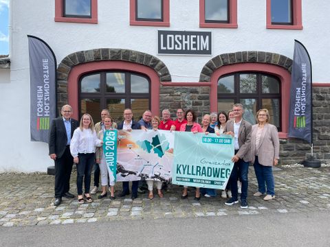 Vertreter der Ortsgemeinden entlang der Strecke und Politiker stehen dicht beeinander und halten das Veranstaltungsbanner hoch.