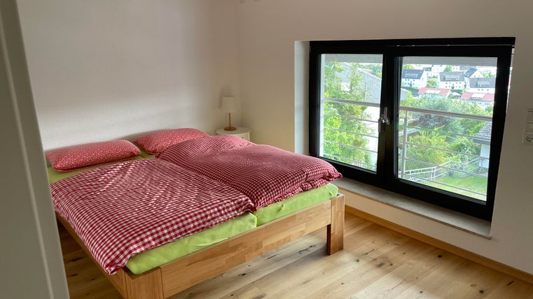 Une chambre lumineuse avec un lit double et des couvertures à carreaux. La fenêtre offre une vue sur les environs et laisse entrer beaucoup de lumière naturelle.