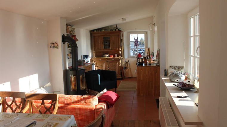 Een gezellige woonkamer met een lichte sfeer. De ruimte is uitgerust met een bank, een tafel en een houtkachel.