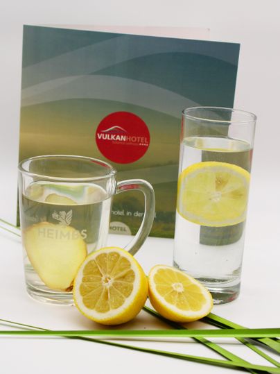 Un verre d'eau avec une tranche de citron et un deuxième verre avec une rondelle de citron sont posés sur une table. En arrière-plan, une brochure d'hôtel est visible.