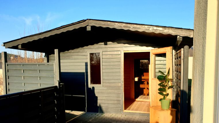 A modern garden house with an open door and a small plant pot inside. The sky is clear and blue, creating an inviting atmosphere.