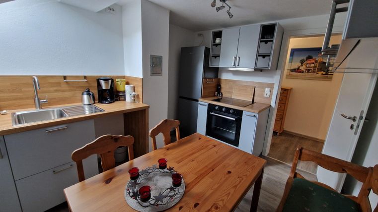 Une cuisine moderne avec des étagères en bois et des meubles blancs. Une table à manger avec un centre décoratif se trouve dans la pièce.