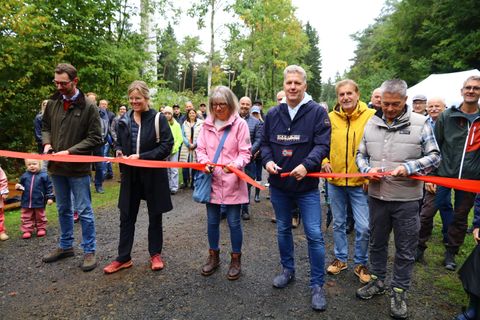 Fünf Personen mit Scheren in den Händen durchschneiden gleichzeitig ein rotes Band. Hinter ihnen zahlreiche Zuschauer und Kinder.
