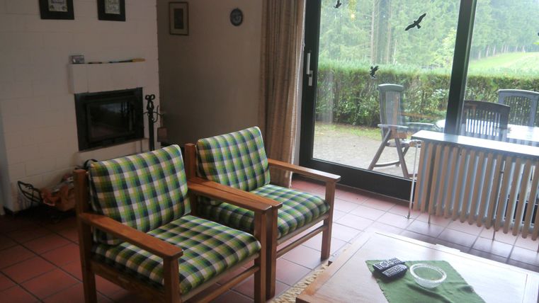 Ein gemütliches Wohnzimmer mit zwei karierten Sesseln und einem Tisch. Große Fenster bieten Blick auf den Außenbereich.